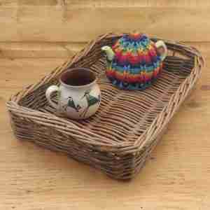 Golden brown rectangular willow tea tray with green sides and handles under the rim, with a rainbow teapot and peacock mug